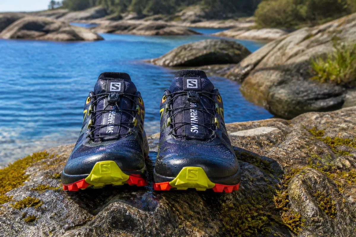 Paire de chaussures de trail techniques pour le swimrun posées sur un rocher humide au bord de l'eau.