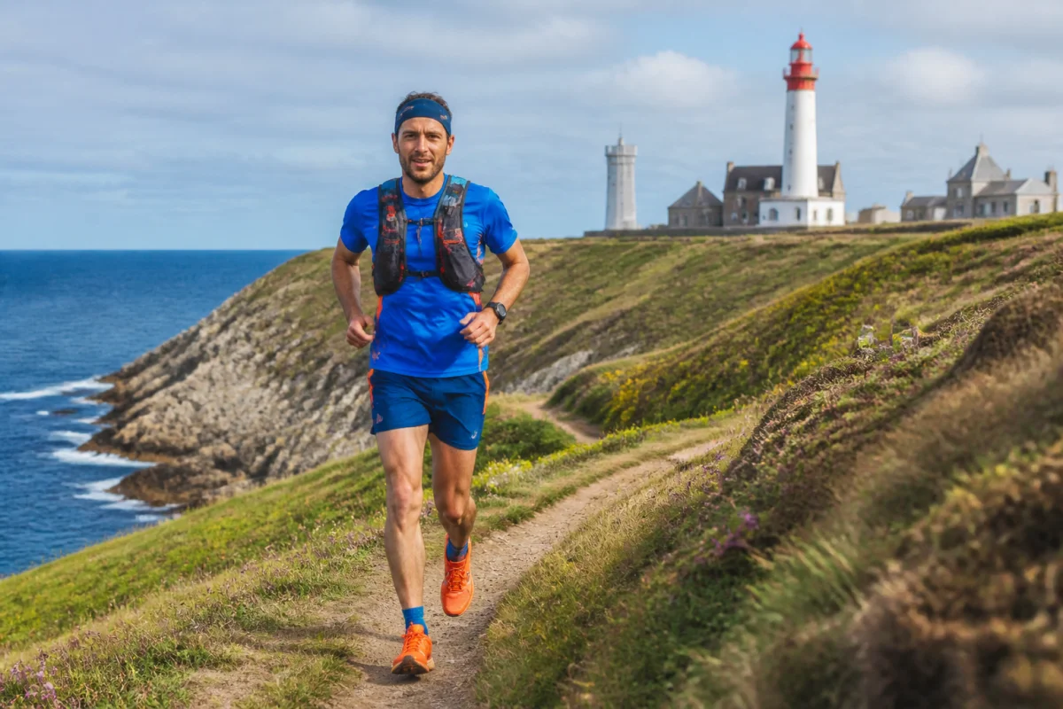 Coureur sur le Trail du Bout du Monde, longeant le GR34 près de la pointe Saint-Mathieu, face à un phare breton